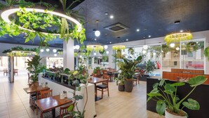 A restaurant interior with multiple dining tables, chairs, hanging plants, and pendant lighting. - Holiday Inn Townsville by IHG (Townsville)