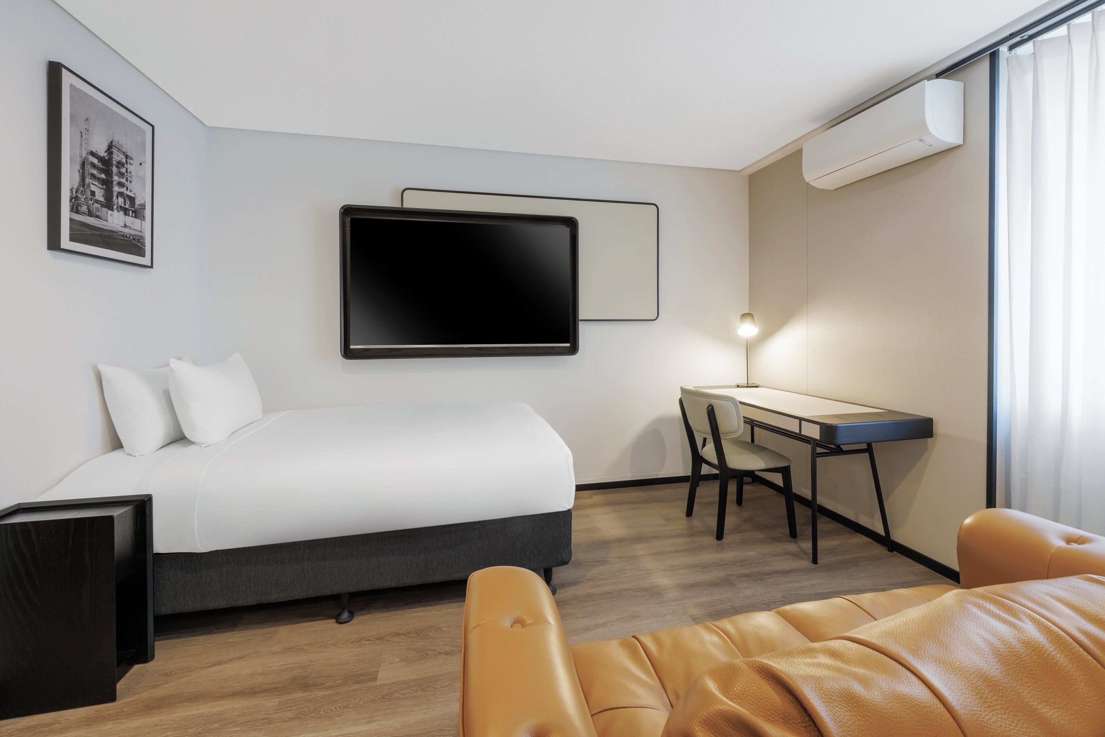 Ein Hotelzimmer mit einem Bett, einem Schreibtisch, einem Stuhl und einem an der Wand befestigten Fernseher.