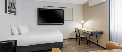 Una habitación de hotel con una cama, un escritorio, una silla y un televisor en la pared.