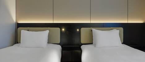 Une chambre d’hôtel avec deux lits simples, une table de chevet et un luminaire fixé au mur.