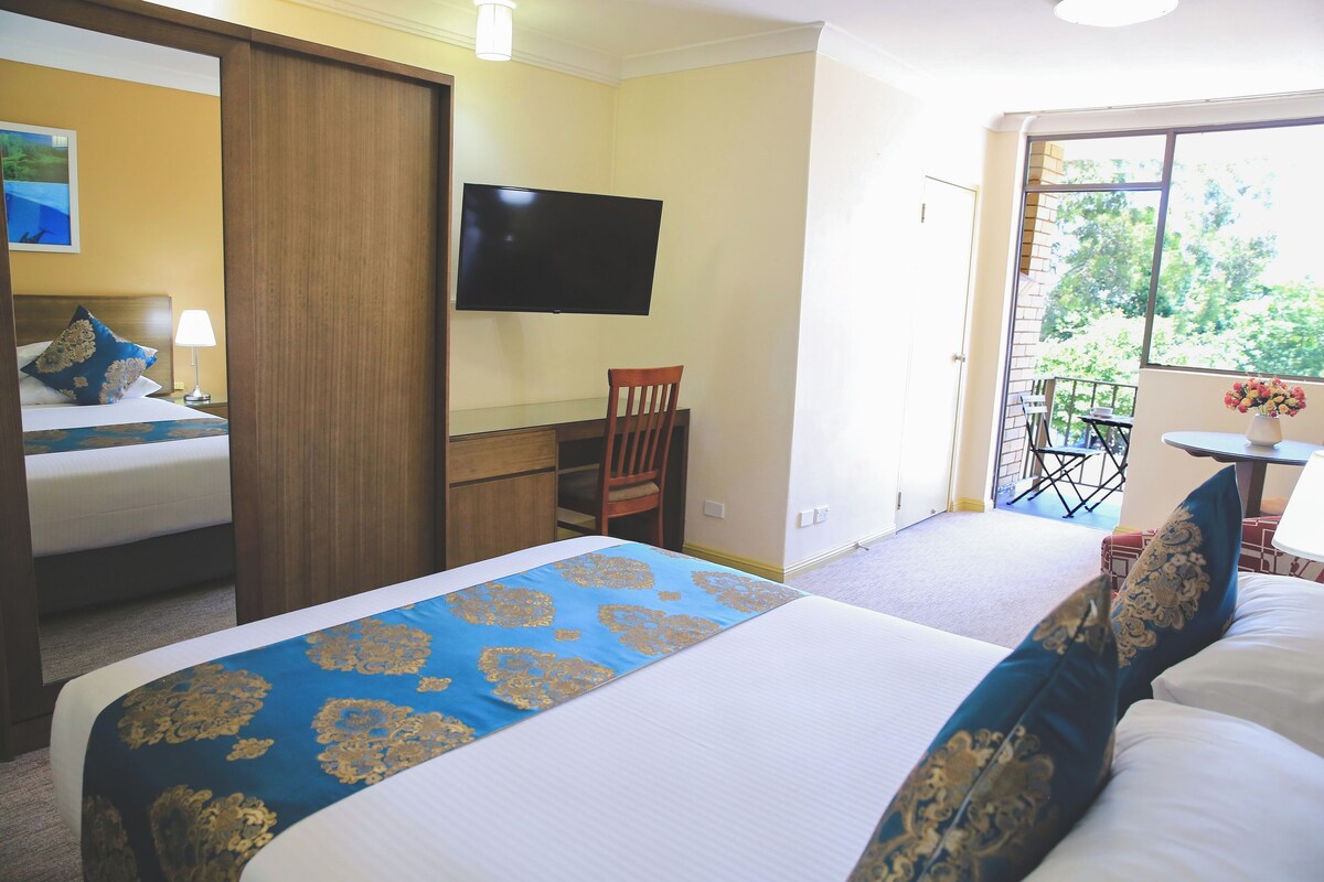 Une chambre d’hôtel comprenant un lit, un bureau, une chaise, une télévision et un balcon avec une table et des chaises.