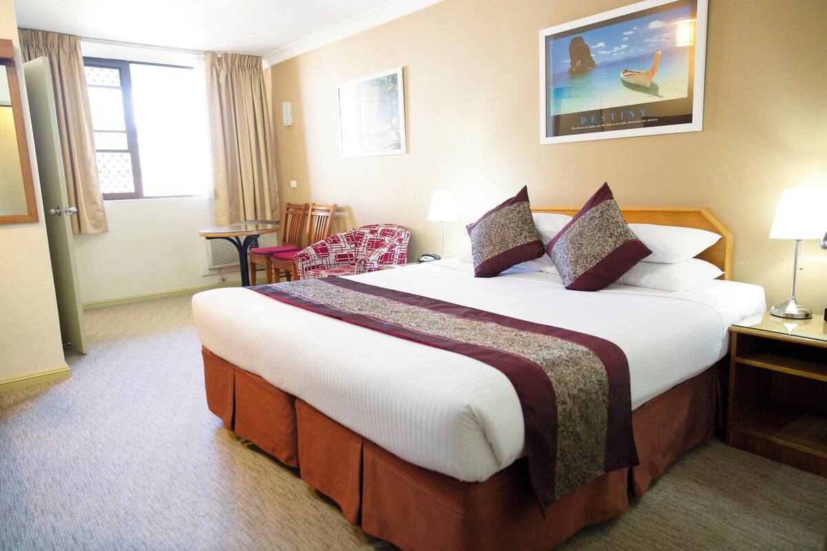 A hotel room with a large bed, a desk, a chair, and a window with curtains.