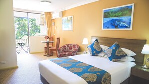 A hotel room with a large bed, a chair, a table, and a balcony with a view of trees. - Ryde Inn (Ryde)