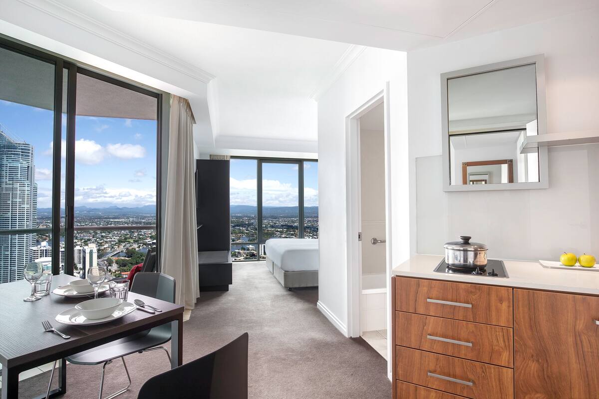 Una habitación de hotel moderna con comedor, cama, vistas a la ciudad y kitchenette.