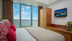A hotel room with a large window, a bed with red and white pillows, a wooden wardrobe, a flat-screen TV, and a vase with flowers. - Mantra Legends Hotel (Surfers Paradise)