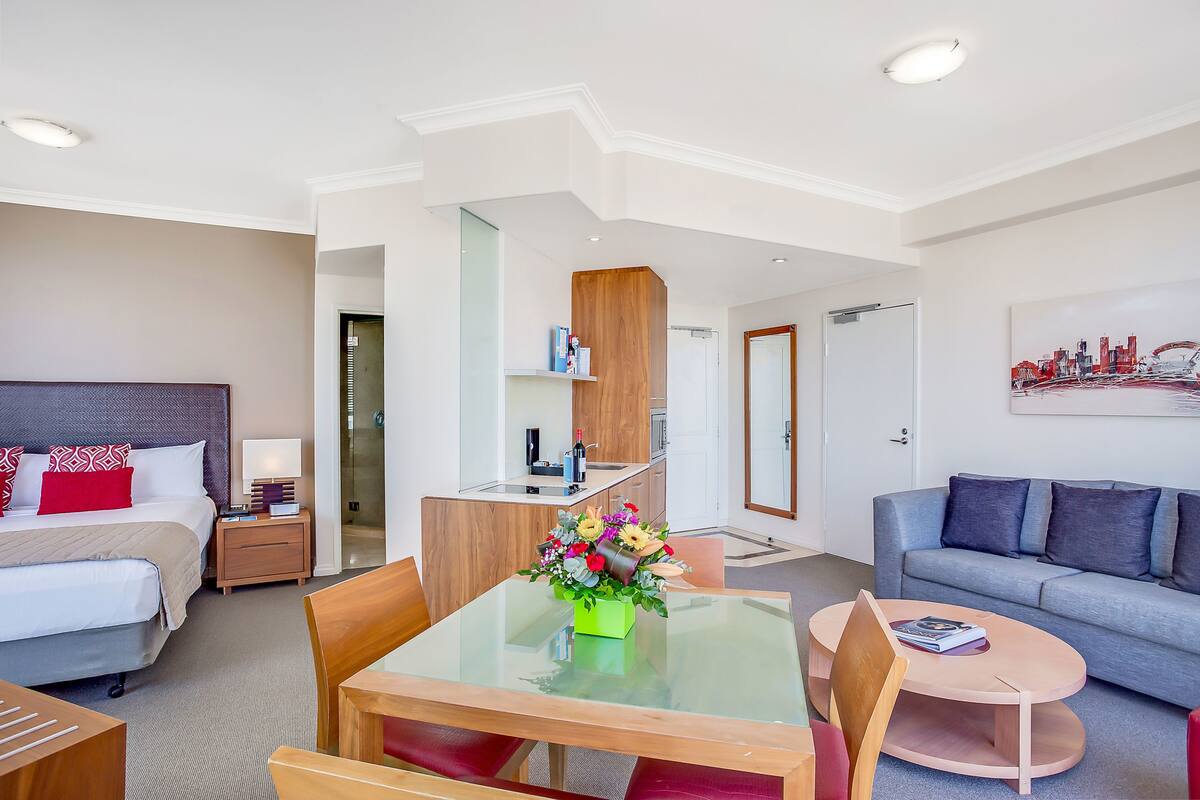 Una habitación de hotel moderna con cama, una mesa de comedor con sillas, un sofá, un pequeño espacio de cocina y una sala de estar.