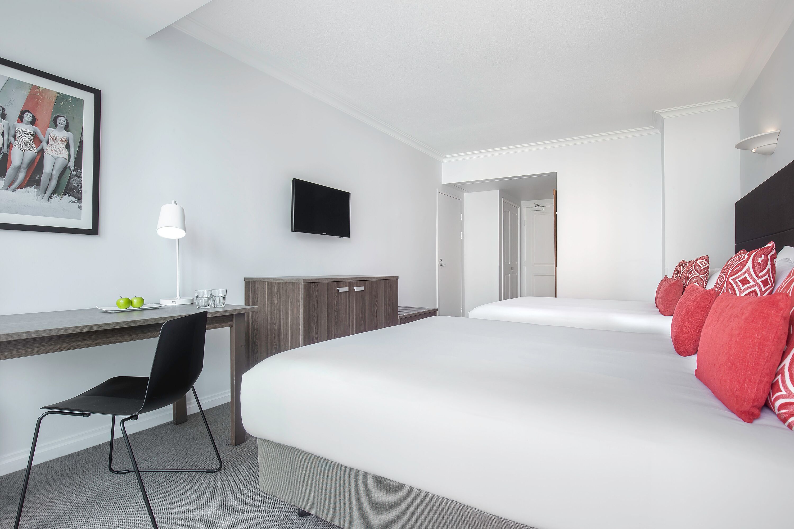 Ein Hotelzimmer mit Bett, Schreibtisch mit Stuhl, Fernseher und einem gerahmten Bild an der Wand.