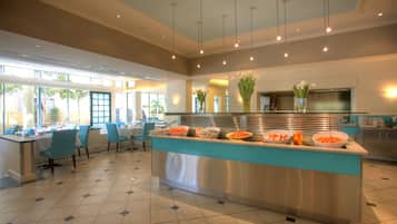 A modern hotel lobby with a central buffet area, seating arrangements, and large windows allowing natural light.