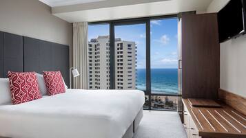 Habitación de hotel con una cama grande, televisión y vistas al océano y edificios.