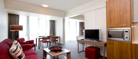 A modern living room with a red sofa, a wooden coffee table, a TV, and a kitchen area with a microwave.
