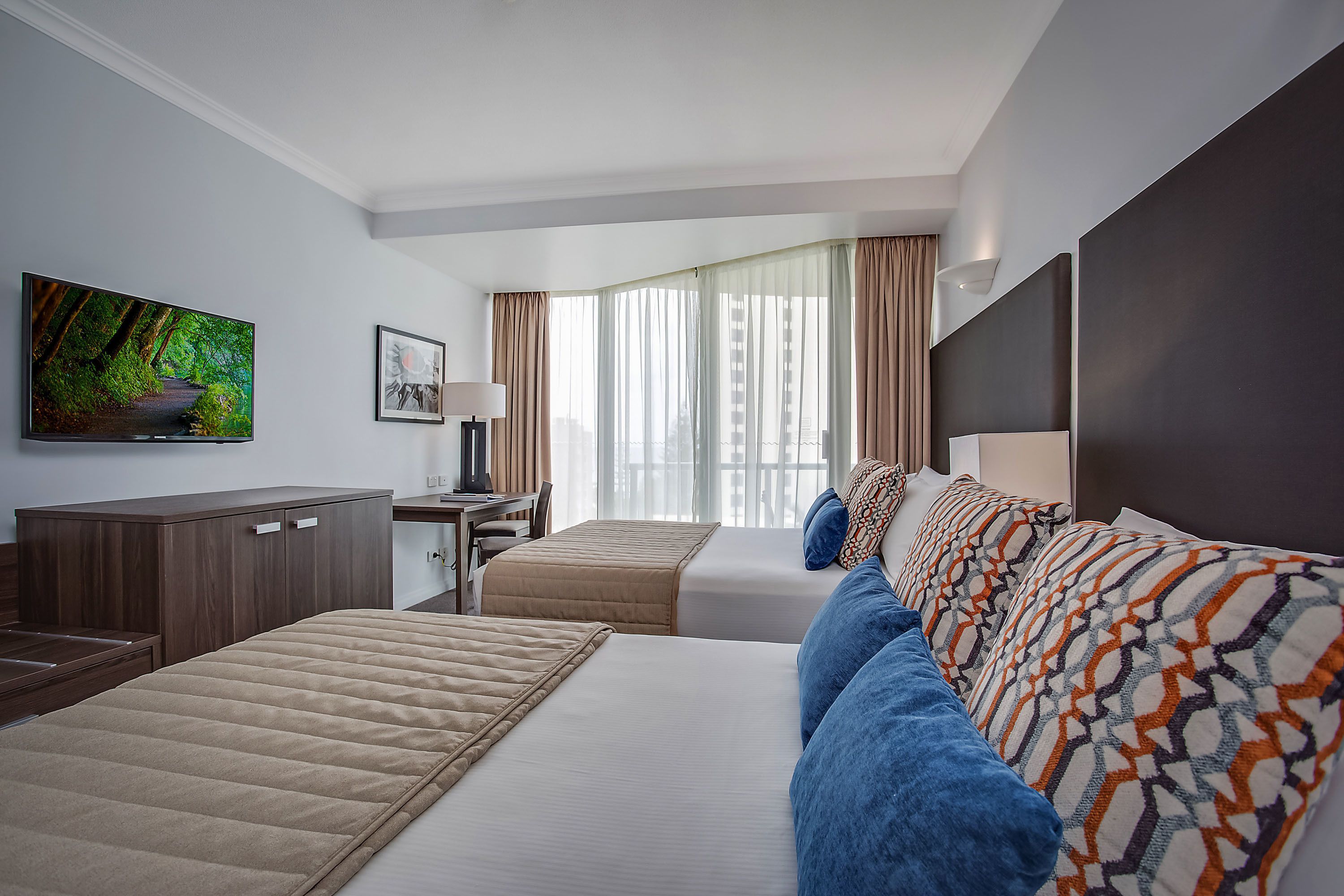 A hotel room with a bed, a desk, a TV, and a view of the city.