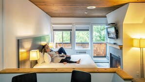 A bedroom with a bed, two bedside lamps, a TV, and a fireplace. - Executive - The Inn at Whistler Village (Whistler)