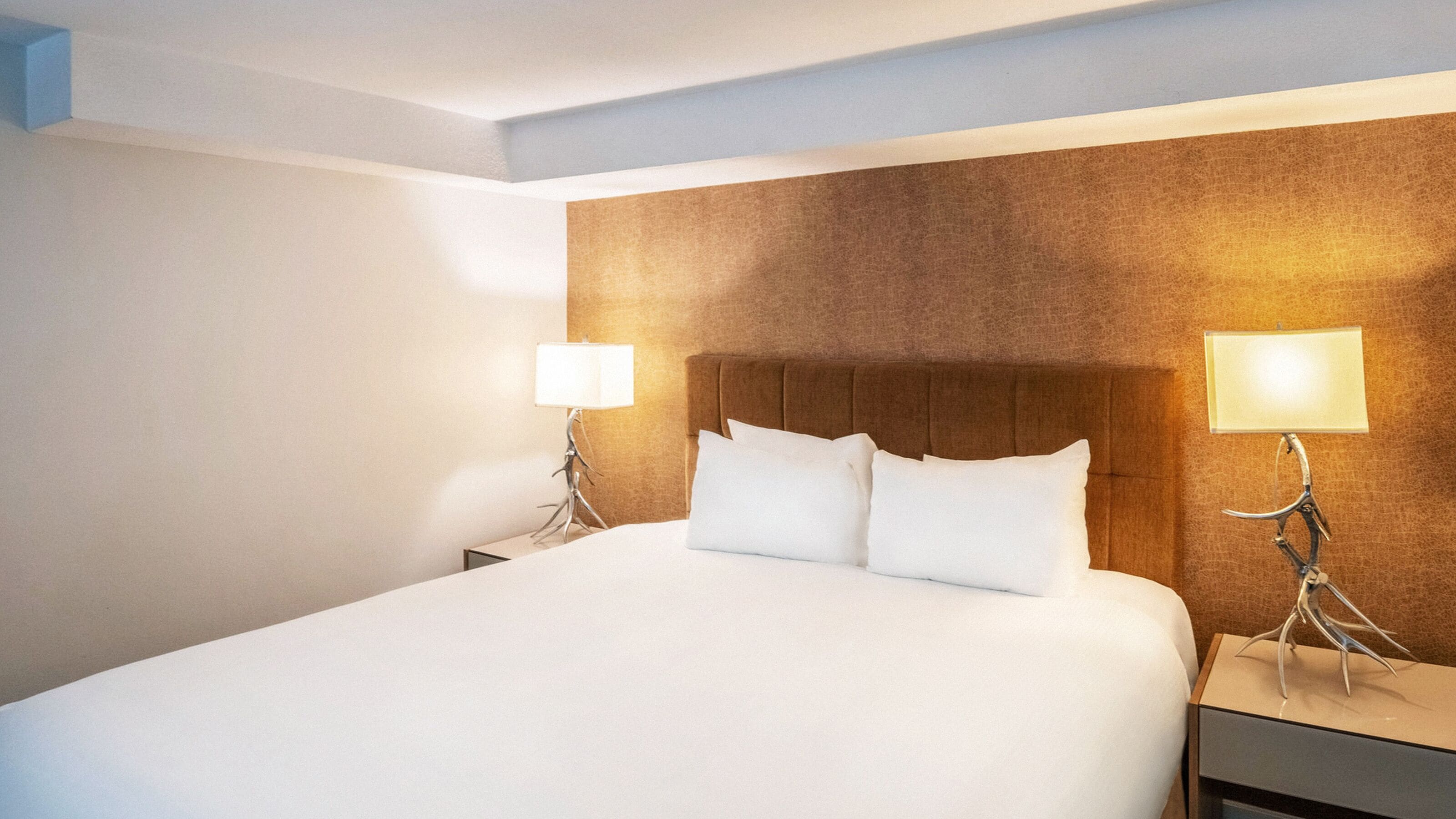 Ein Hotelzimmer mit einem großen Bett, zwei Nachttischen mit Lampen und einem Holzkopfteil.