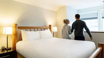 Habitación de hotel con una cama grande, dos lámparas de noche, una mesita de noche con un reloj y una ventana con vistas al exterior.