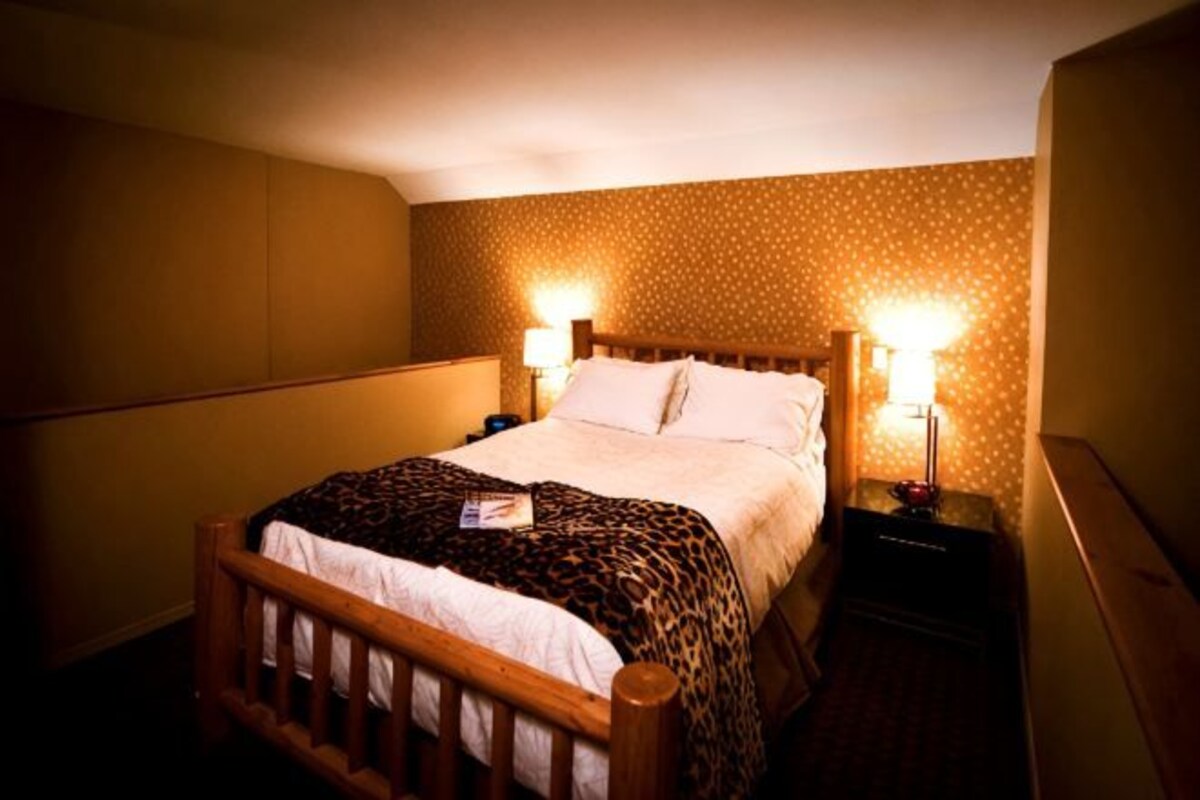 Una habitación de hotel con una cama, dos lámparas de noche, una mesita de noche y una manta de estampado de leopardo.