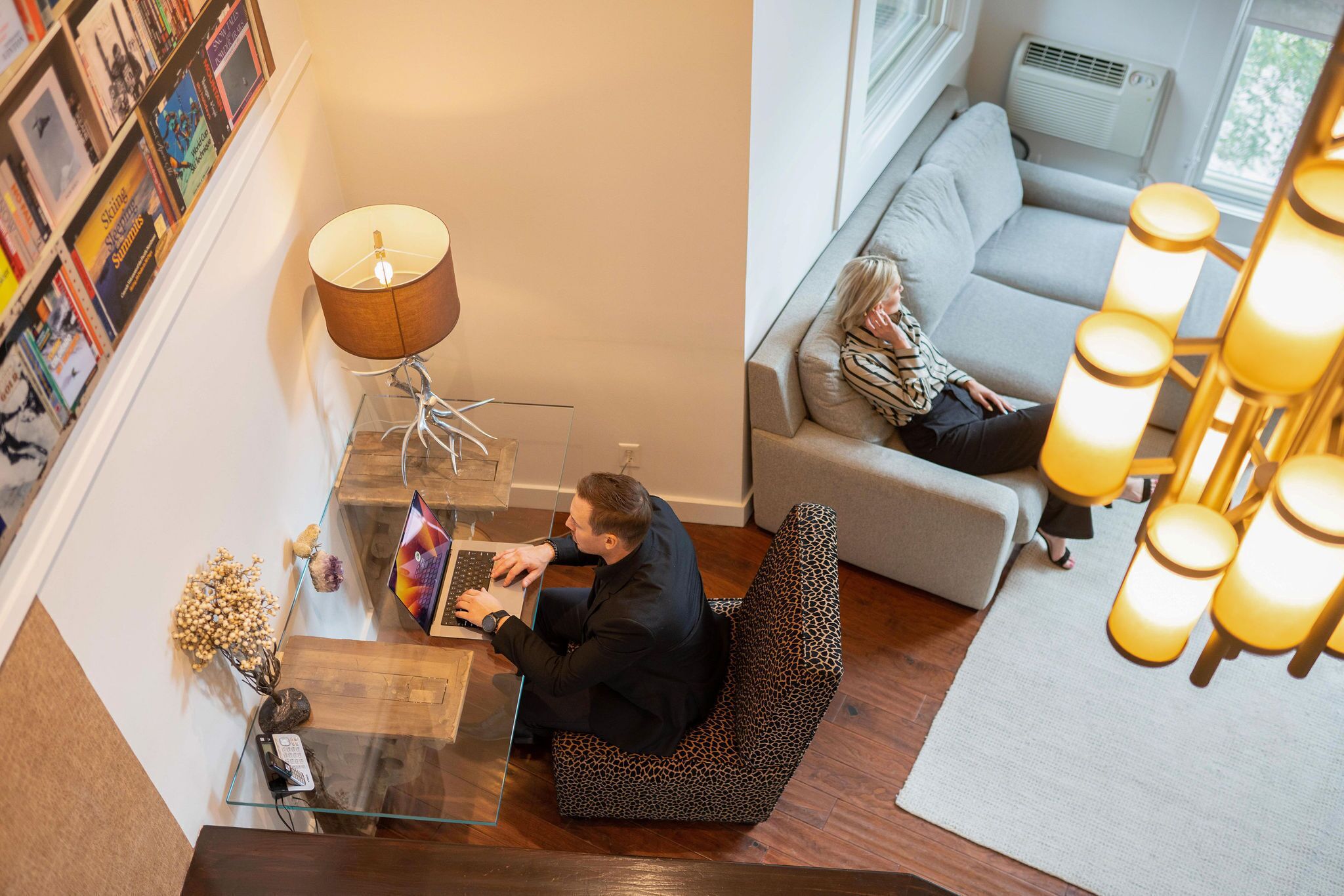 A modern living room with a glass coffee table, a leopard print chair, a sofa, and a bookshelf filled with books.