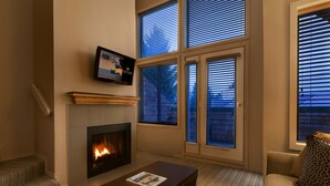 A living room with a fireplace, a television mounted on the wall, and a sofa with a leopard print pillow. - Executive - The Inn at Whistler Village (Whistler)
