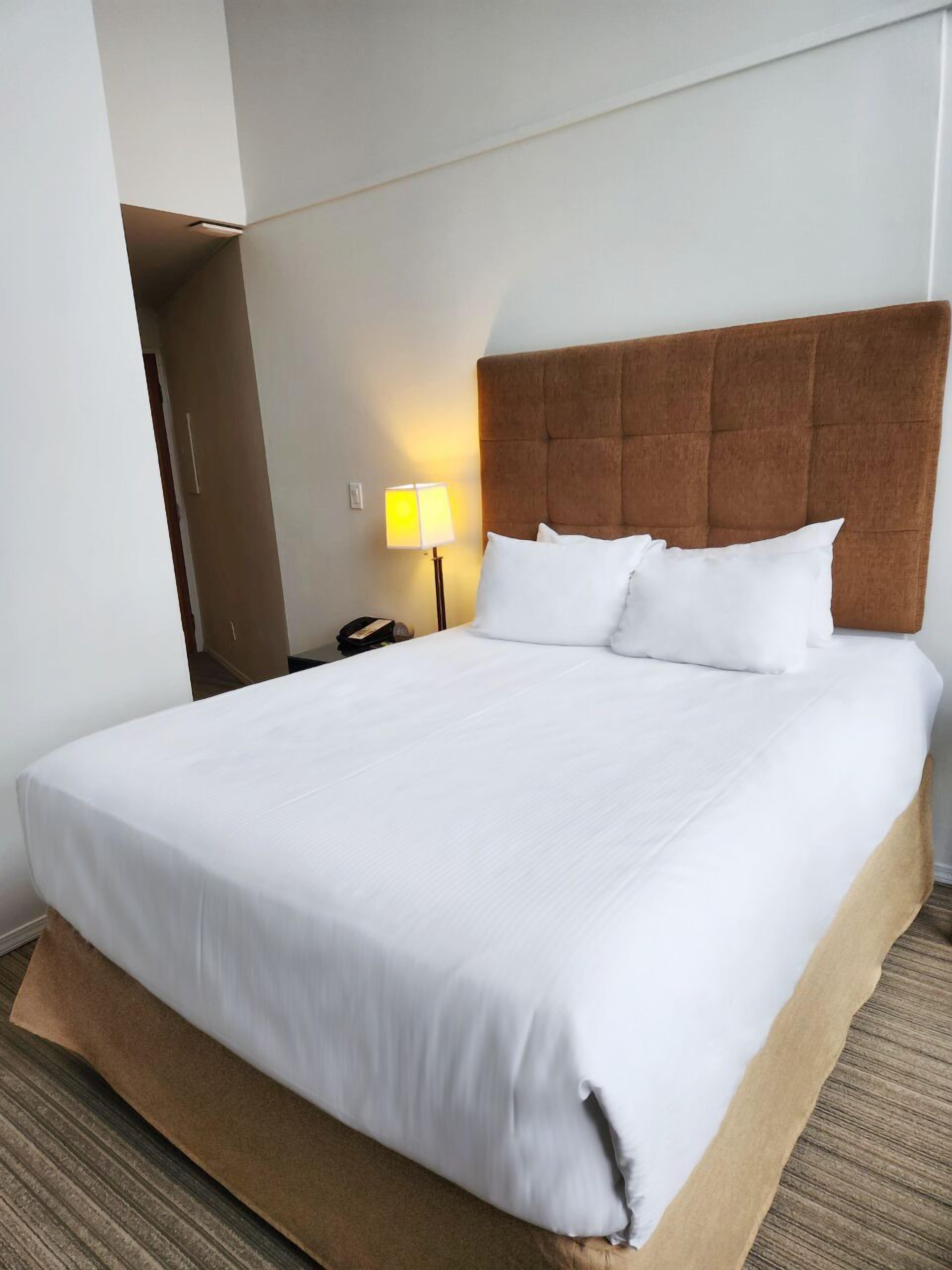 Una habitación de hotel con una cama grande, un cabecero, una mesita de noche y una lámpara.