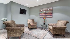 Une pièce comprenant trois fauteuils, un tapis à motifs, un téléviseur à écran plat et un tableau abstrait aux couleurs vives accroché au mur.