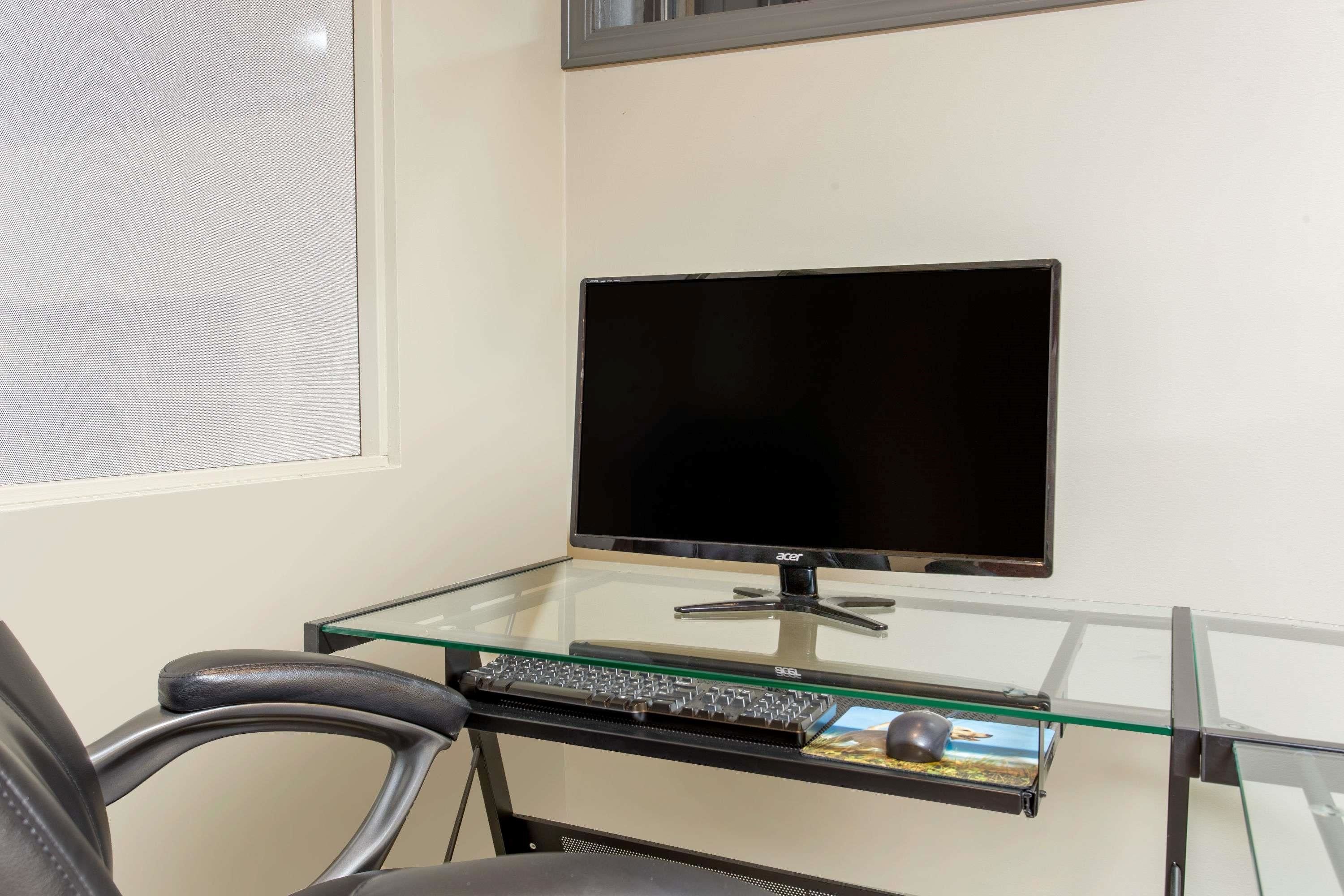 Un bureau en verre avec un écran, un clavier et une souris noirs.