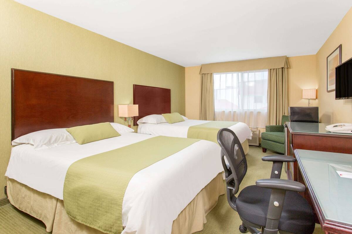 Een hotelkamer met twee bedden, een bureau, een stoel, een televisie en een raam met gordijnen.