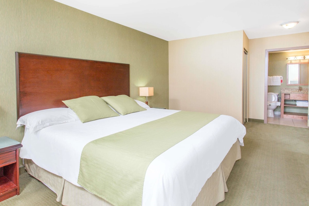 Hotelkamer met een groot bed, nachtkastje, lamp en een badkamer zichtbaar door een open deur.