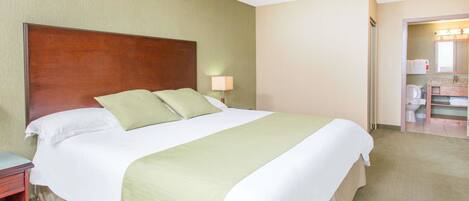 A hotel room with a large bed, a nightstand, a lamp, and a bathroom visible through an open door.