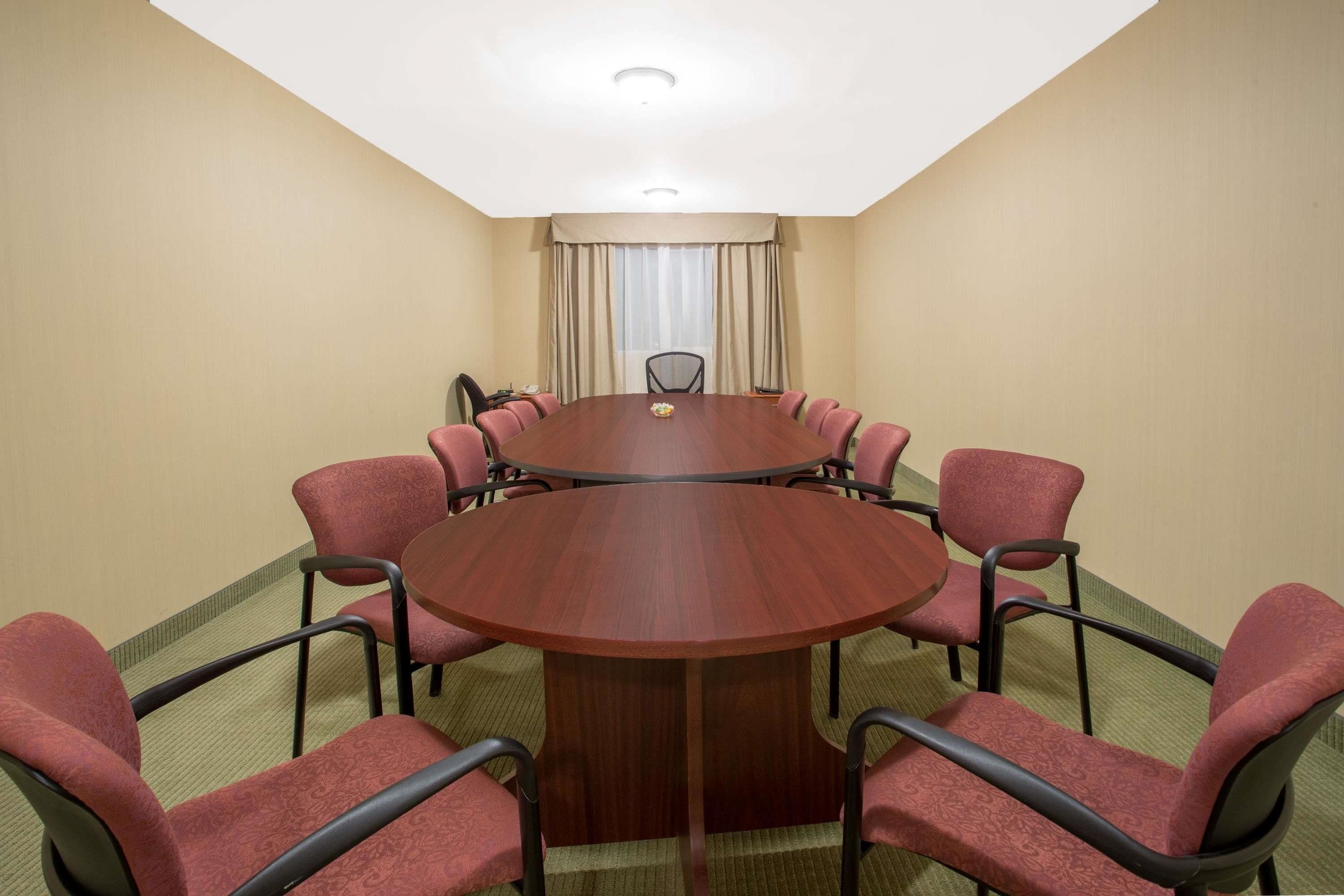 A conference room with a round table, red upholstered chairs, and a carpeted floor.