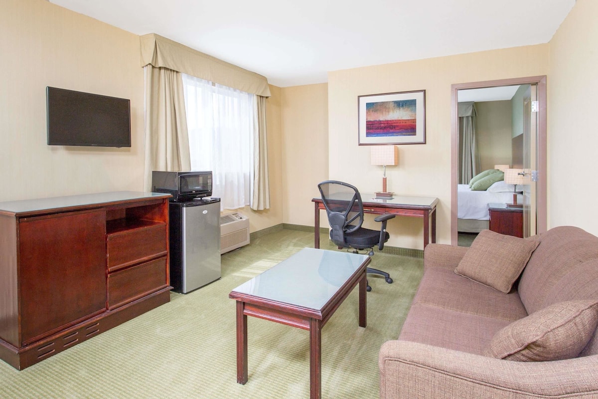 Een hotelkamer met een houten bureau, een televisie, een bank en een bed met een groen kussen.