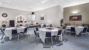 Une salle de conférence avec des tables et des chaises rondes, un écran de projection et une horloge au mur.