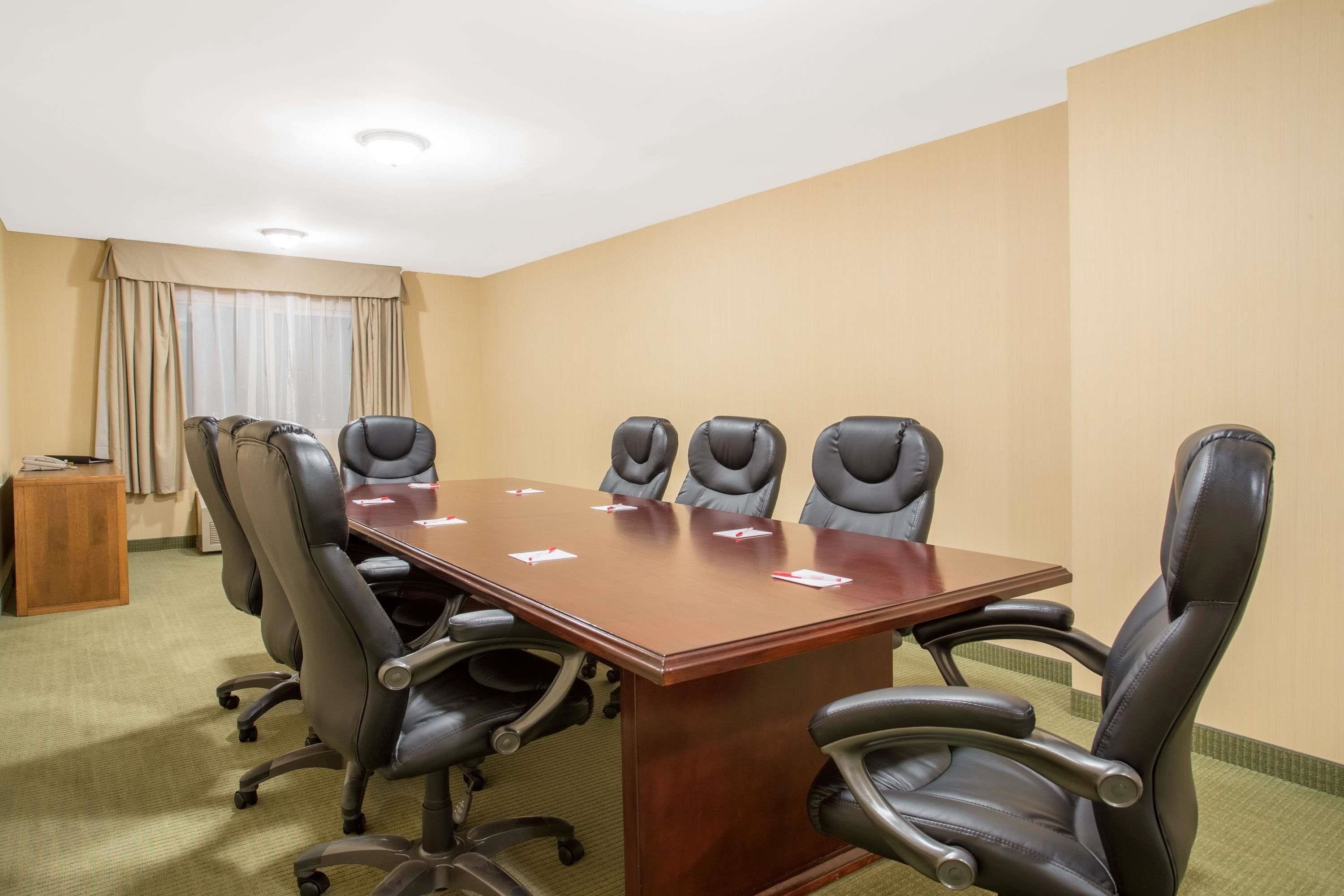 Un salón de conferencias con una amplia mesa de madera, seis sillas de cuero negro y un pequeño mueble de madera.