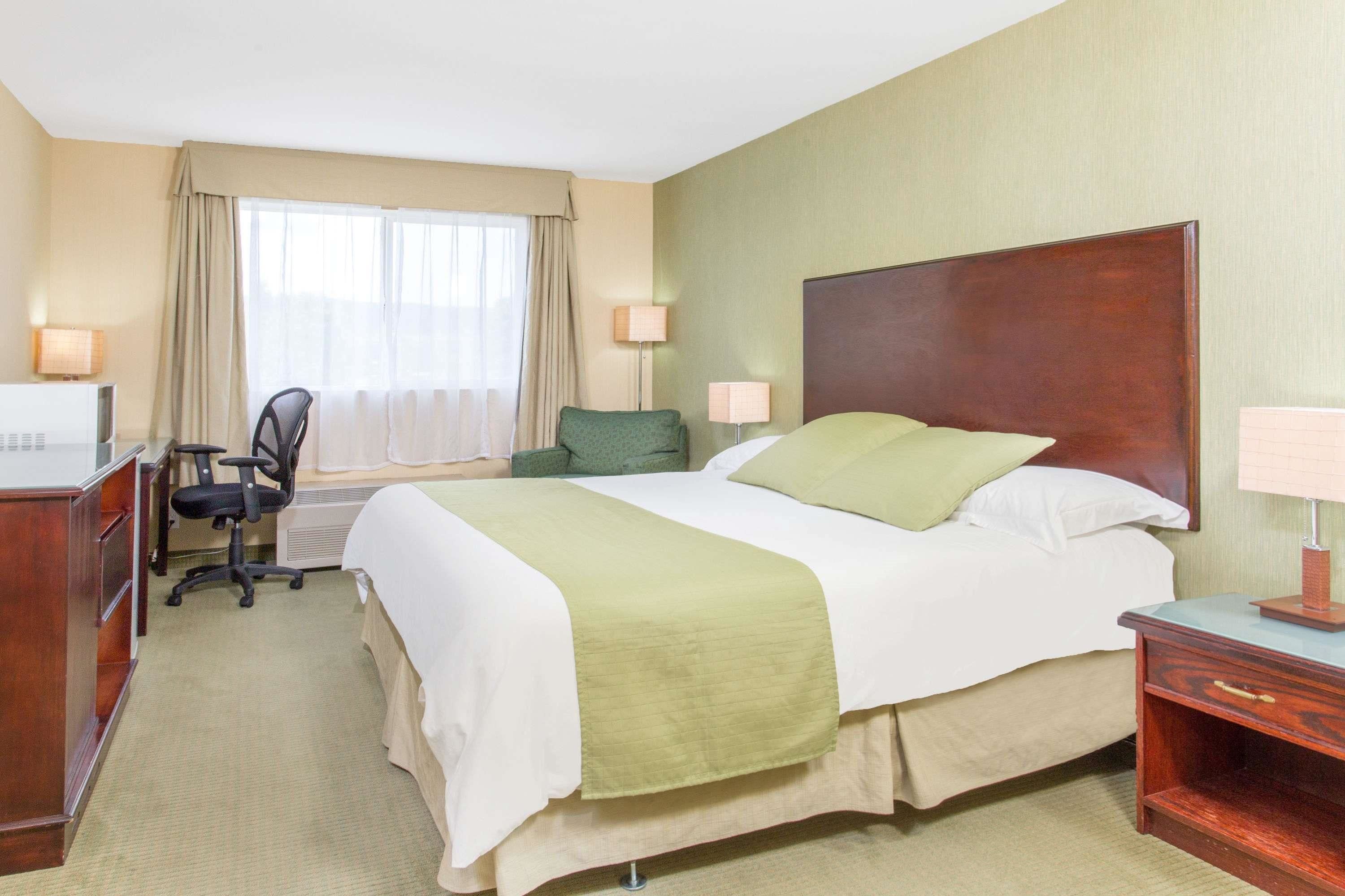 A hotel room with a bed, desk, chair, and two lamps.