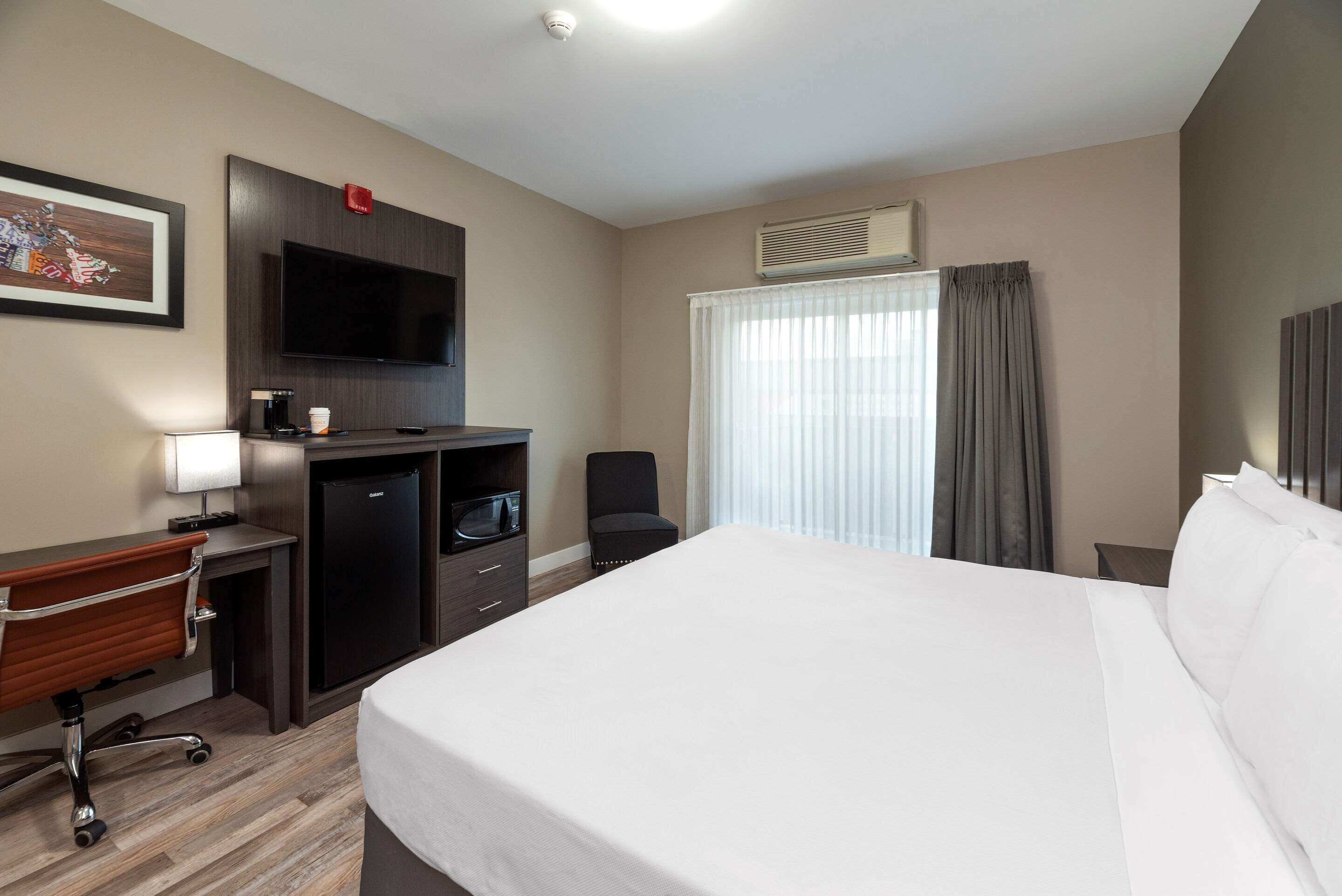 A hotel room with a bed, desk, chair, TV, and a window with curtains.