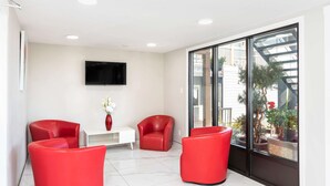 A modern room with two red chairs, a white table, and a TV on the wall. - Econo Lodge (Prince George)