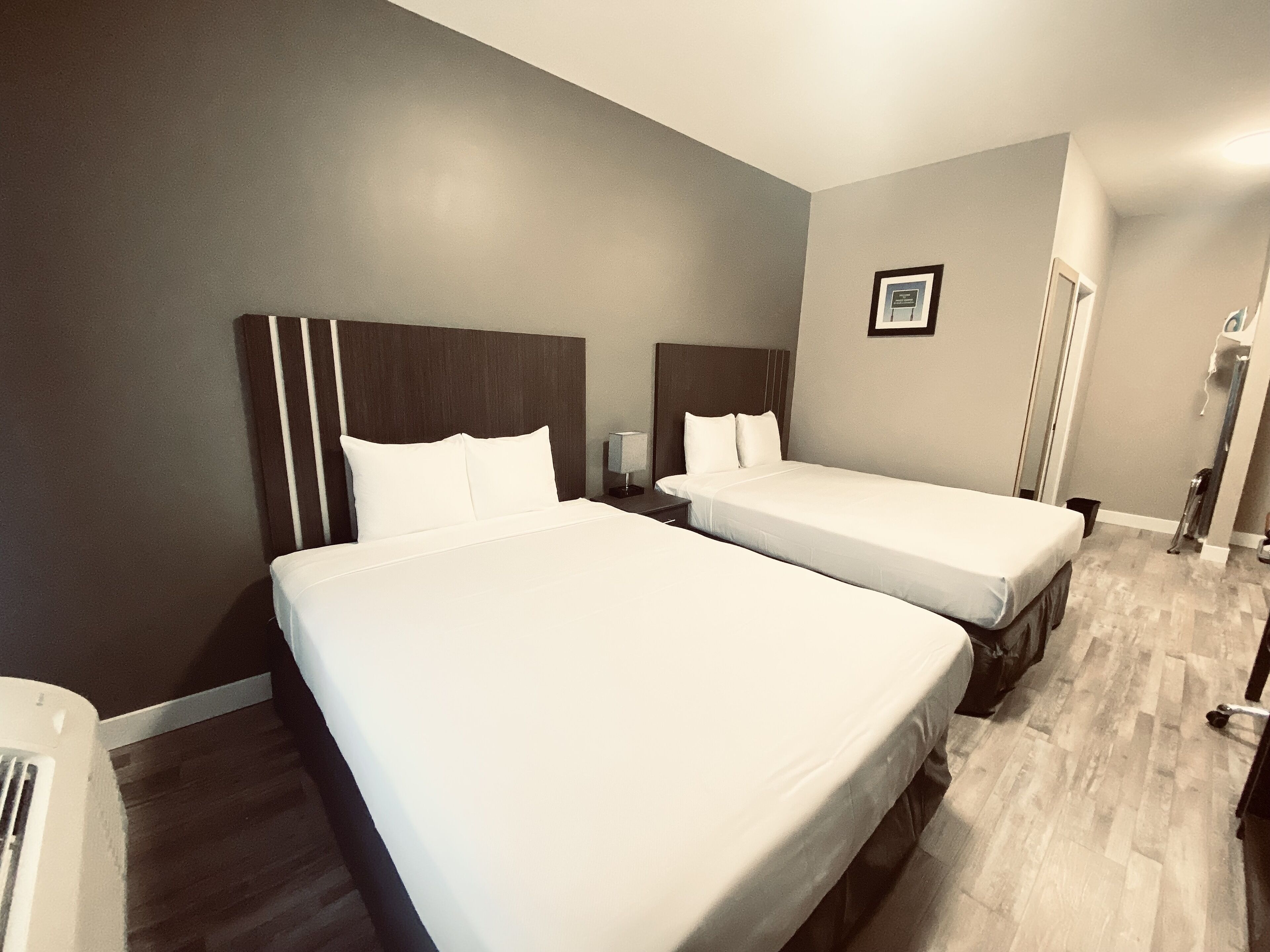 A hotel room with two single beds, a nightstand, a framed picture on the wall, and a wooden floor.