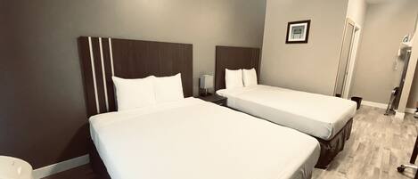 A hotel room with two single beds, a nightstand, a framed picture on the wall, and a wooden floor.
