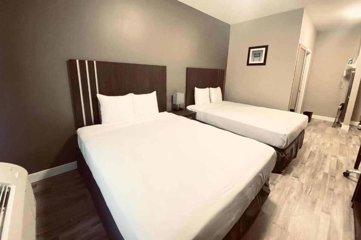 A hotel room with two beds, a wooden floor, and a neutral color scheme.