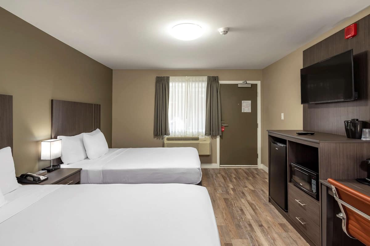 Quarto de hotel com duas camas, uma mesa de trabalho com televisão, micro-ondas e uma pequena cozinha.