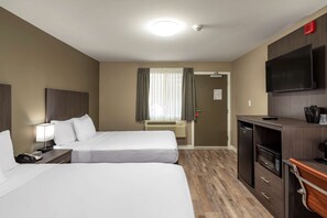 A hotel room with two beds, a desk with a TV, a microwave, and a small kitchenette.