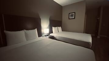 A hotel room with two single beds, a nightstand with a lamp, and a framed picture on the wall.