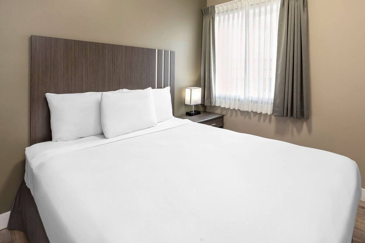Cama bem arrumada com lençóis brancos e cabeceira de madeira.