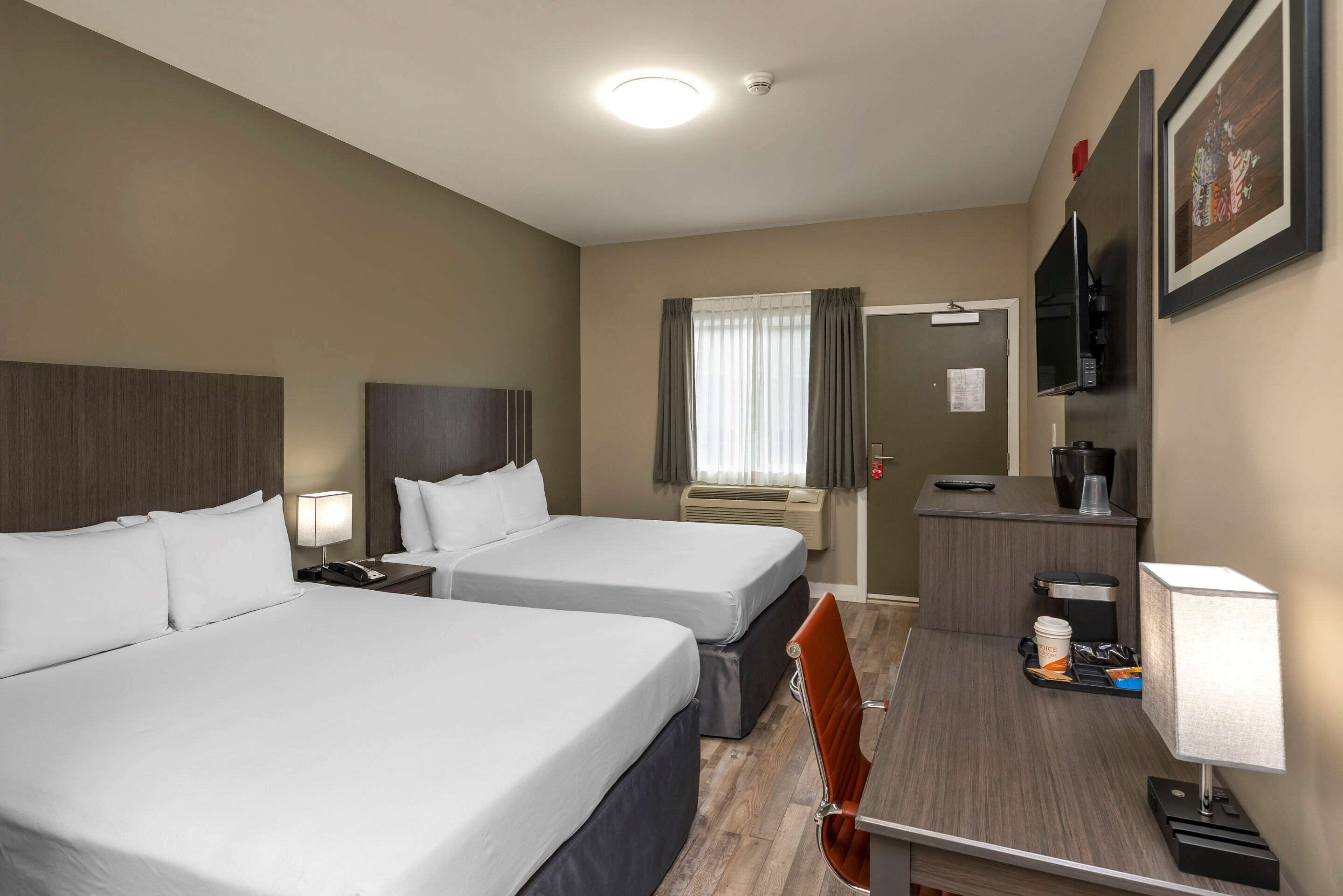 A hotel room with two beds, a desk with a chair, a television, and a coffee machine.