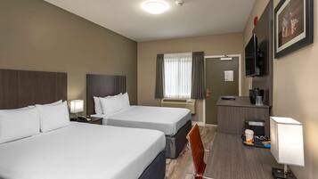 A hotel room with two beds, a desk with a chair, a television, and a coffee machine.