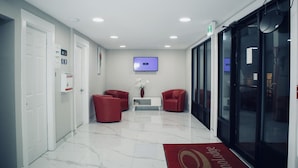A modern lobby with a flat-screen TV, two red chairs, a vase with white flowers, and a red carpet with a logo. - Econo Lodge (Prince George)