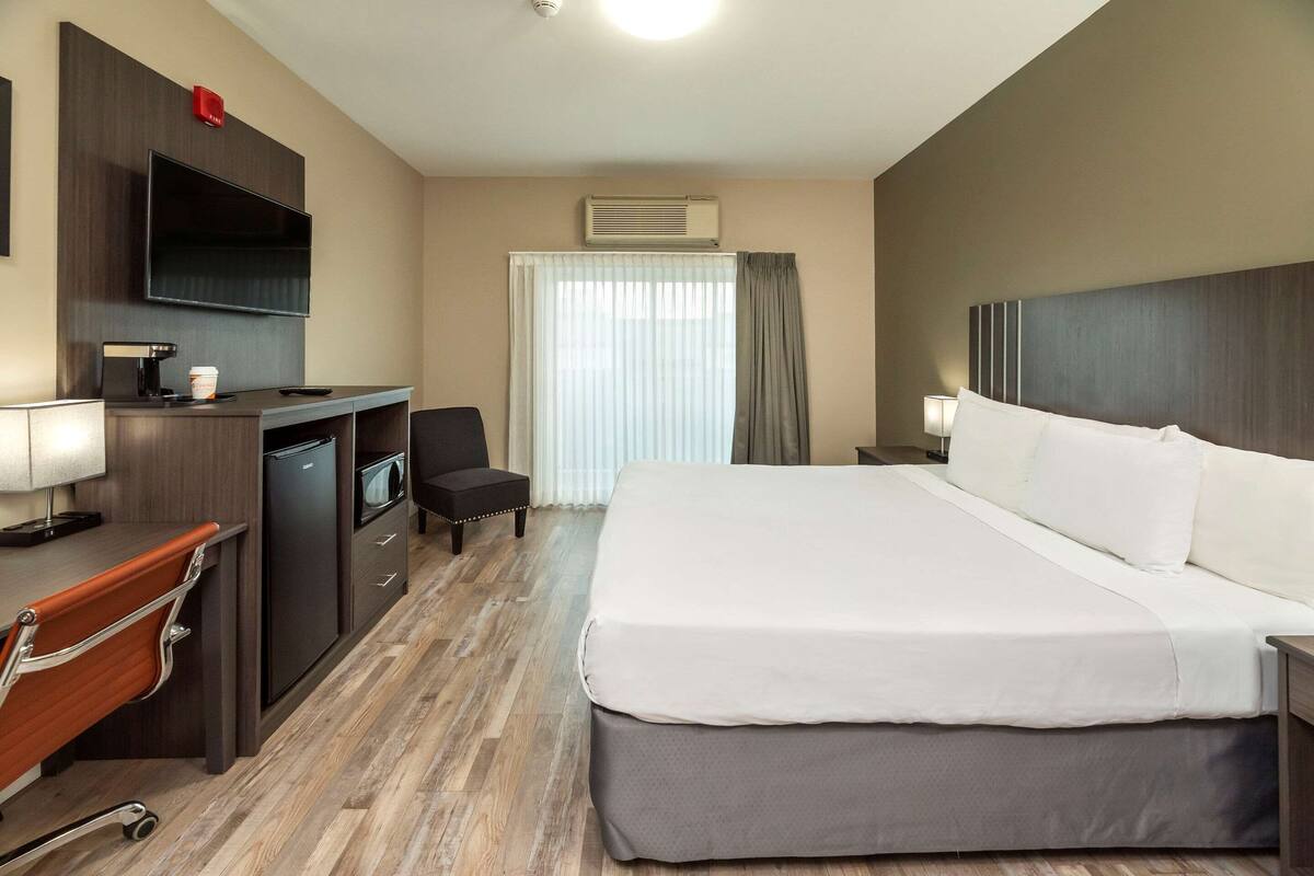 Quarto de hotel com cama, escrivaninha, cadeira, televisão e ar condicionado.