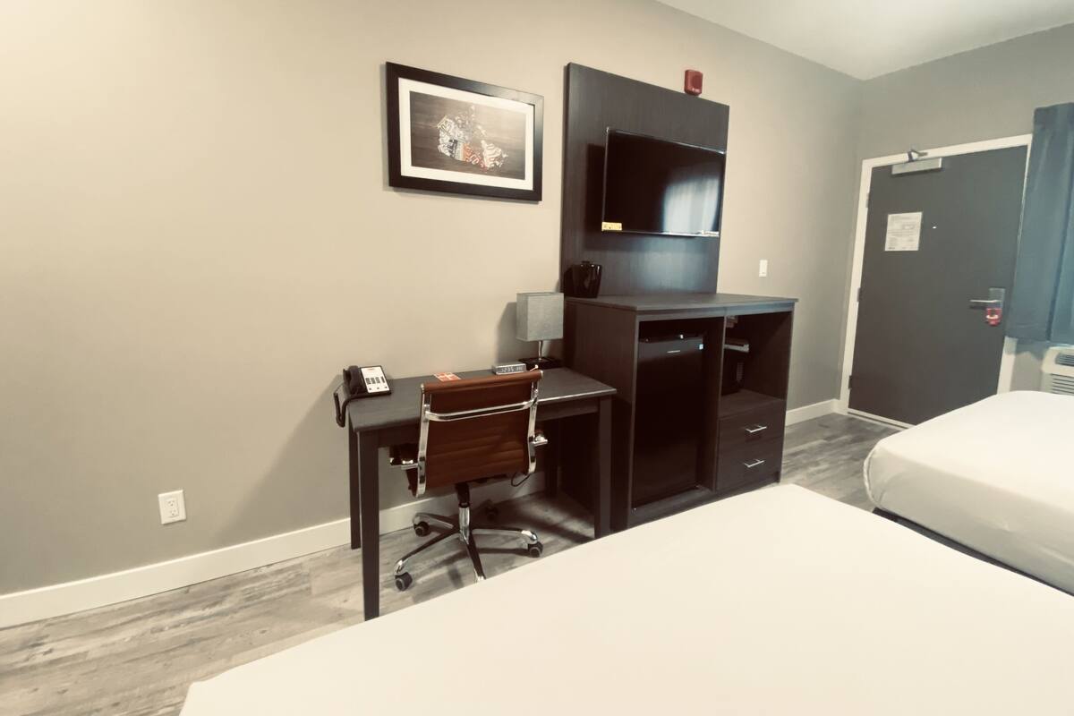Quarto de hotel com uma cama, uma escrivaninha com cadeira, televisão e porta.