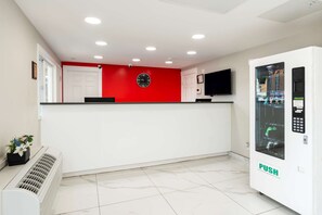 A reception area with a red accent wall, a clock, a flat-screen TV, and a vending machine labeled "PUSH".