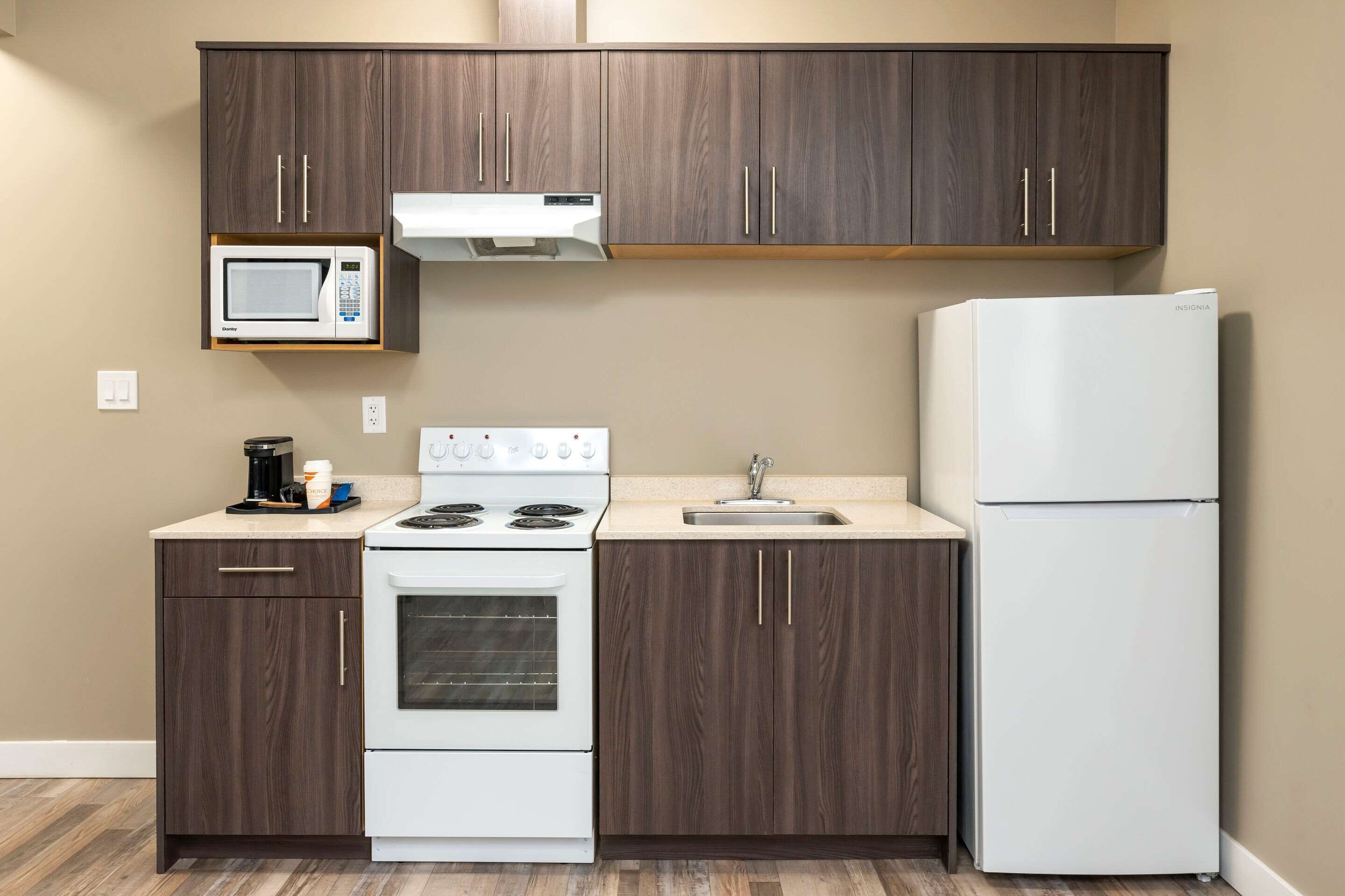 A kitchen with dark wood cabinets, a white stove, a microwave, and a refrigerator.