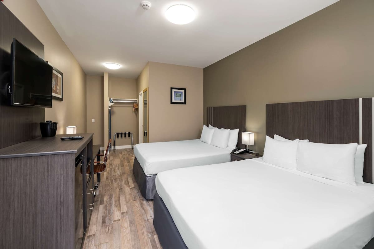 Quarto de hotel com duas camas, uma televisão, uma escrivaninha com cadeira e um espelho.