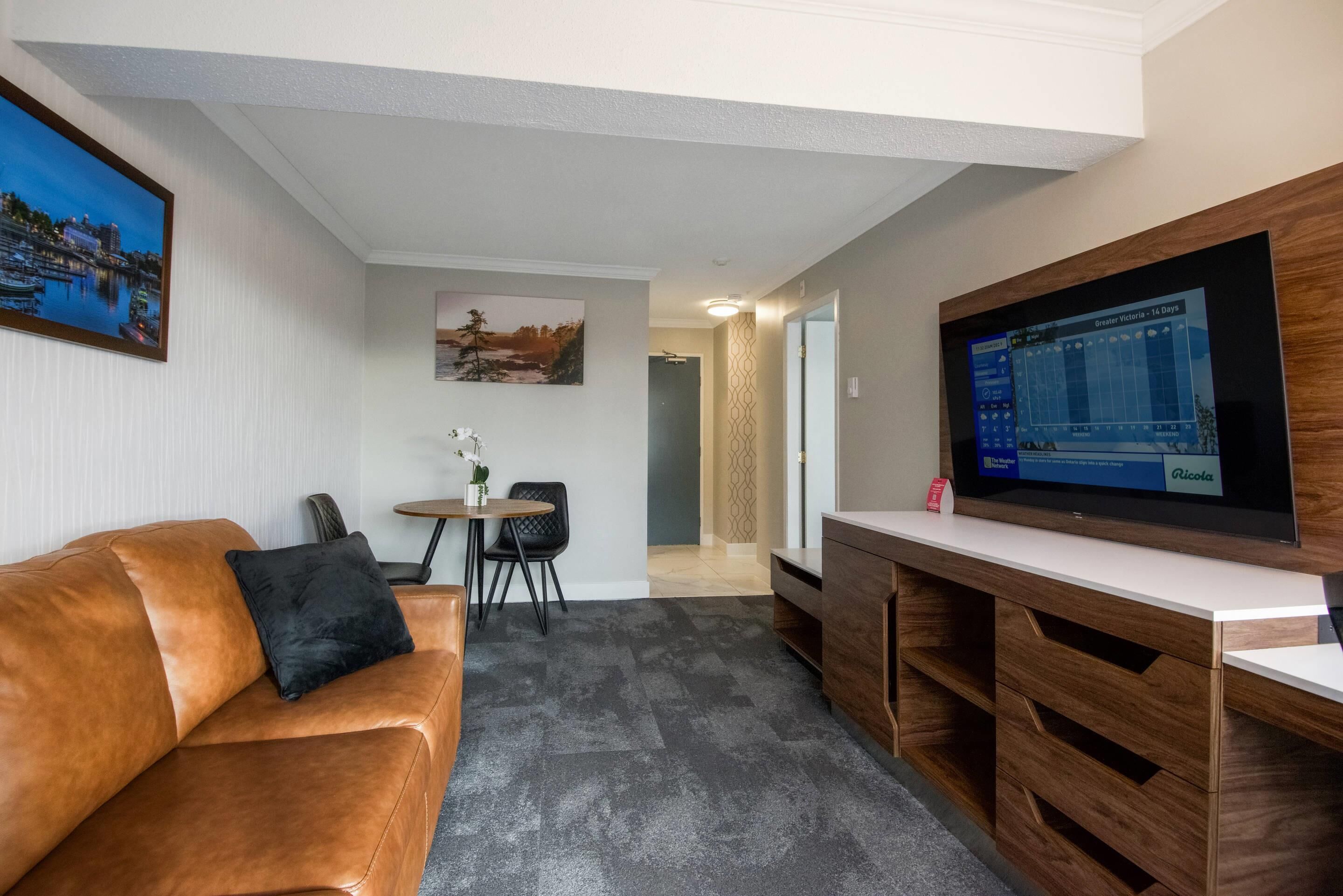 A living room with a leather sofa, a small table with chairs, a flat-screen TV, and a wall-mounted TV.